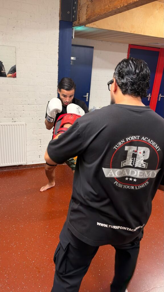 Een kickbokser oefent met een coach op stootkussens bij Turning Point Academy.