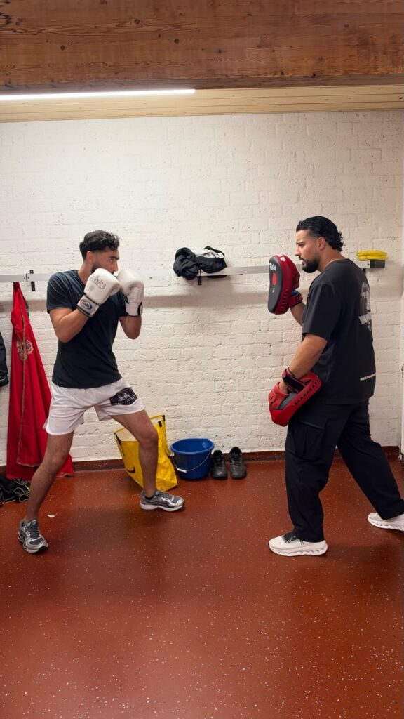 Een kickbokser en coach oefenen tegenover elkaar met bokshandschoenen en stootkussens.