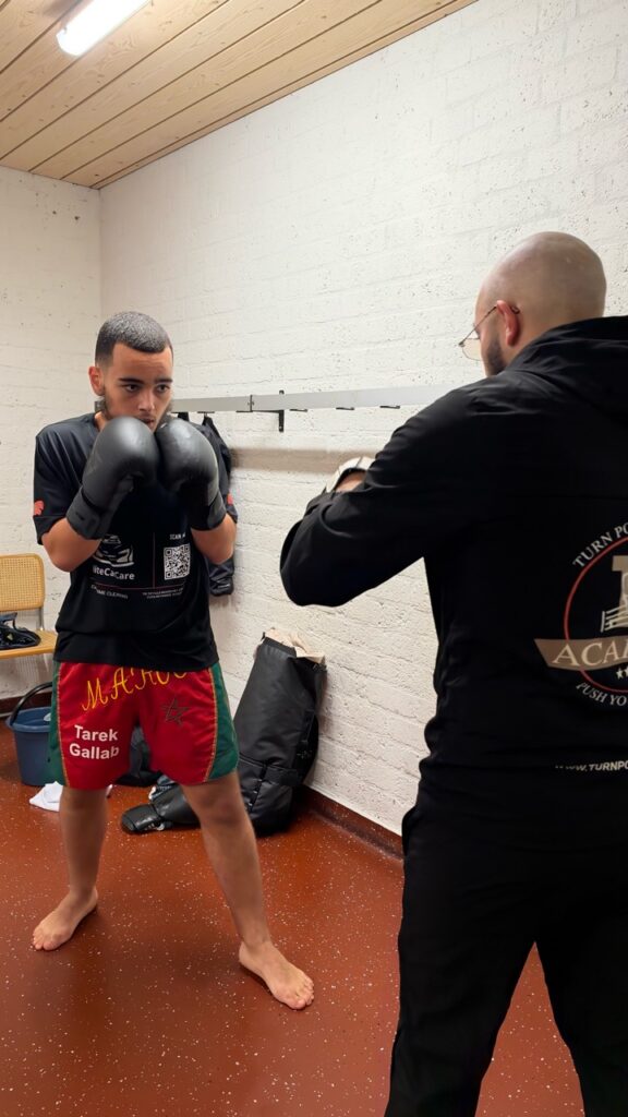 Een kickbokser houdt zijn dekking omhoog tijdens een oefening met de coach.